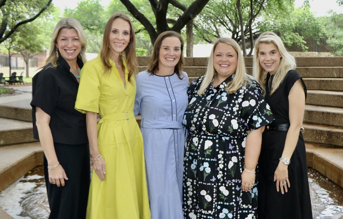 Five members of the Parent Faculty Association (PFA) Board stand together outdoors beside a small water feature, smiling at the camera. The group is dressed in professional attire and posed in a landscaped courtyard with trees and tiered stone seating in the background.